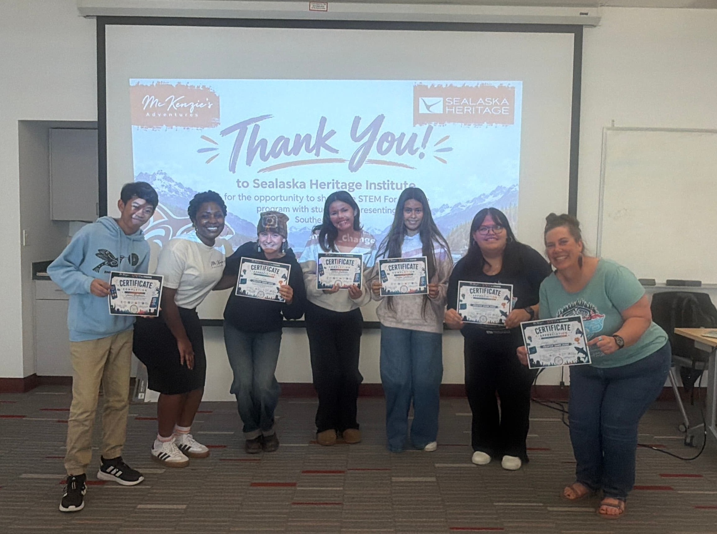 Students and program leaders hold STEM for Change certificates in front of a 'Thank You' slide to Sealaska Heritage Institute in Juneau, Alaska.